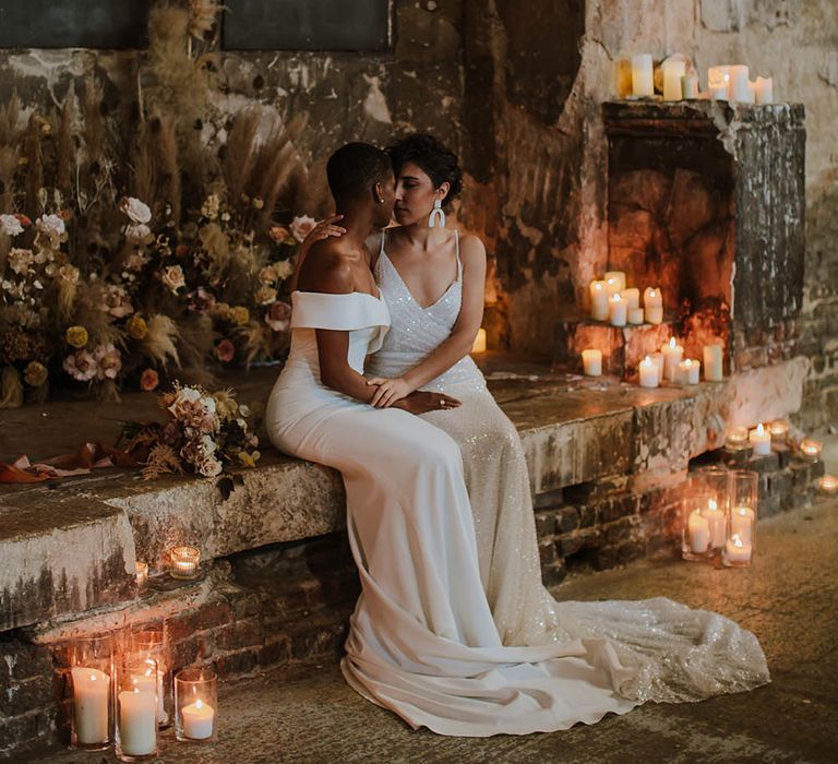 Two brides kissing at The Asylum London wedding venue altar surrounded by church candles and dried flowers 