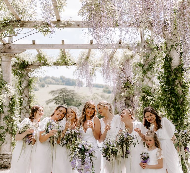 Bride stands with her bridesmaids beneath pergola at the West Dean Gardens