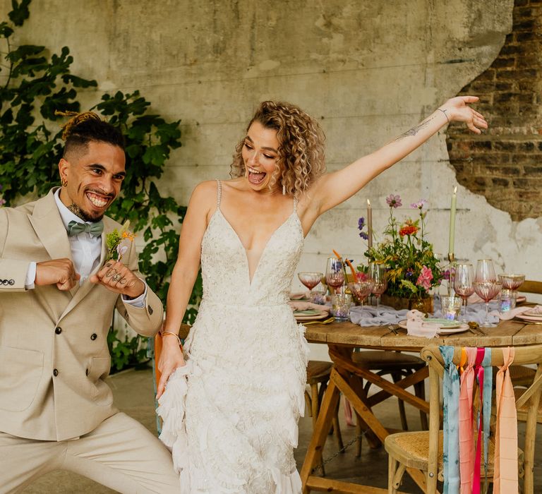 Bride in a fitted wedding dress with straps and groom in a beige suit celebrating at their colourful fiesta theme wedding 