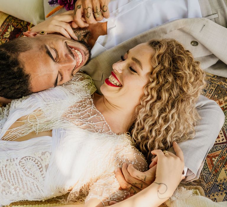 Blonde curly haired bride with bright red lipstick laying on wool rugs with her groom at their fiesta theme wedding 