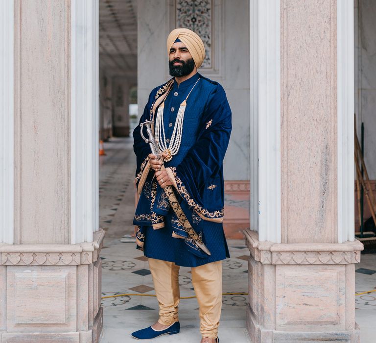 Groom stands outside the Guru Nanak Darbar whilst wearing royal blue 