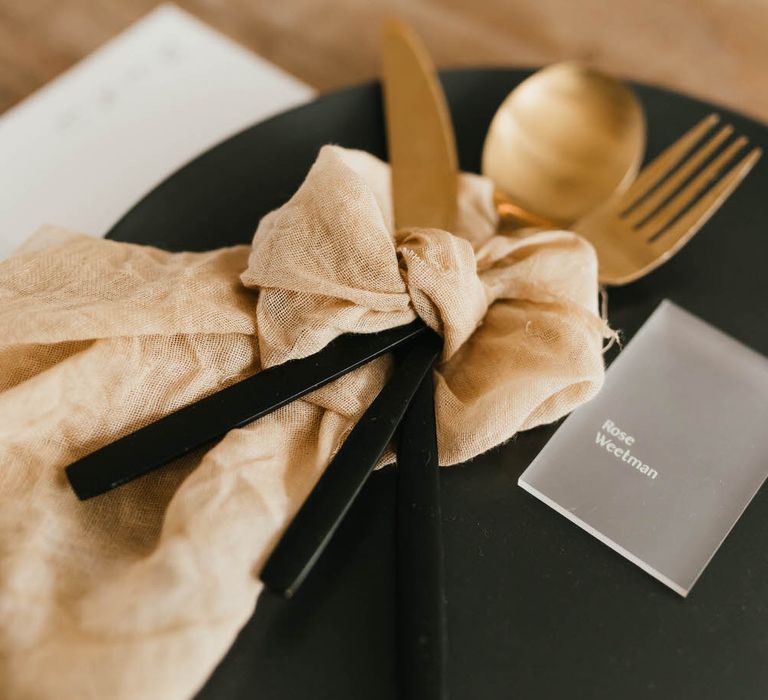 Neutral linen napkin tied around gold cutlery on a black plate