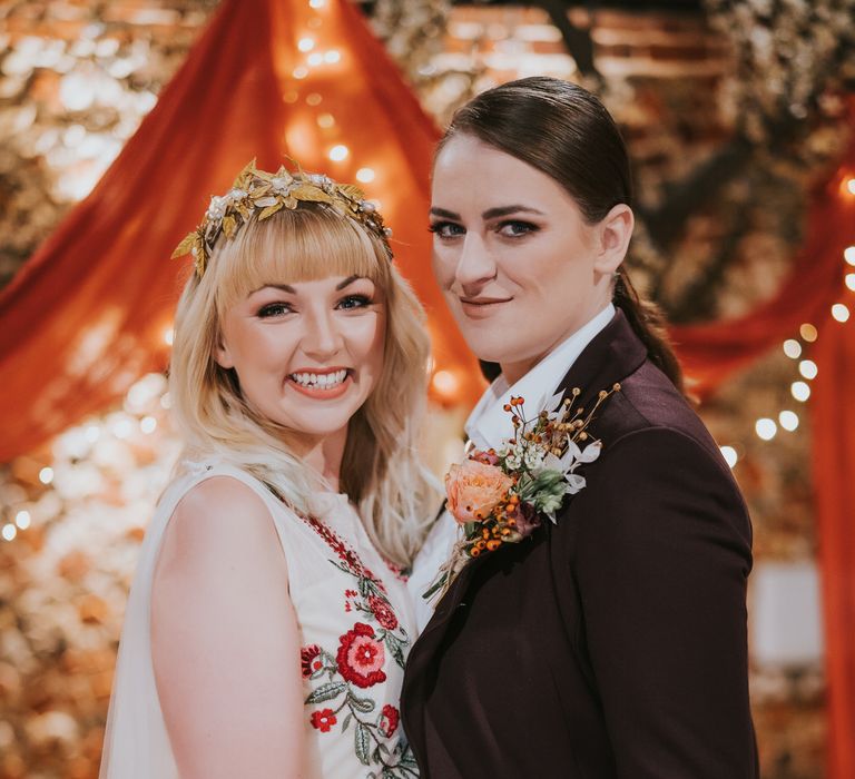 Two brides hugging and looking to camera in front of blossom trees