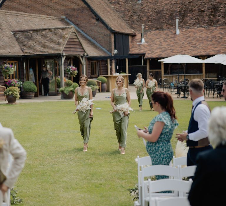 Bridesmaids in green satin dresses walking down the aisle at outdoor wedding ceremony at Cooling Castle Barn 