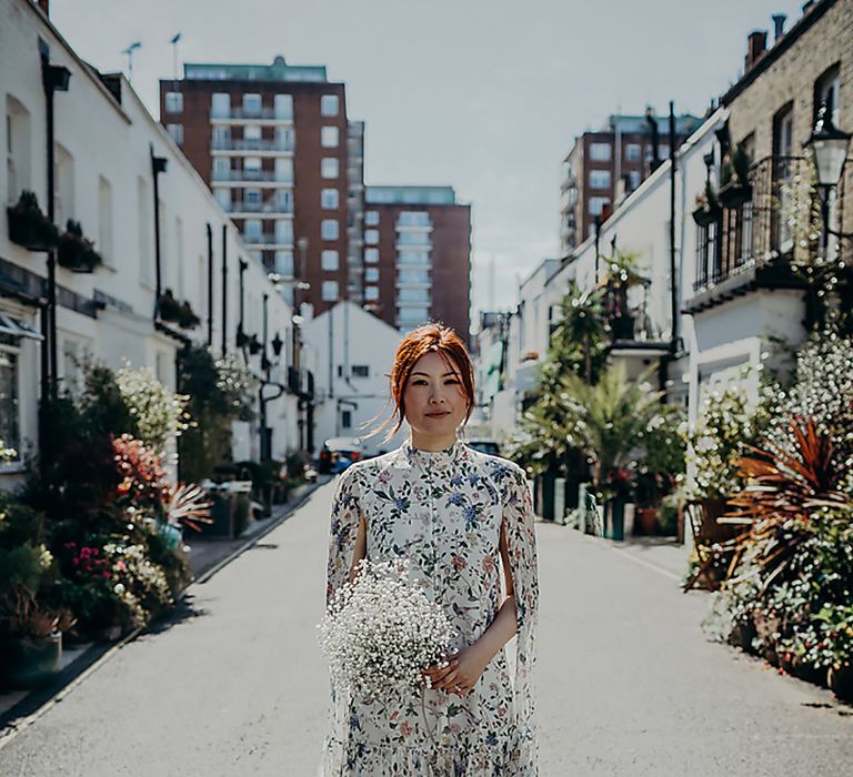 Stunning East Asian bride in a short wedding dress with blue floral design and long cape sleeves holding a white gypsophila wedding bouquet