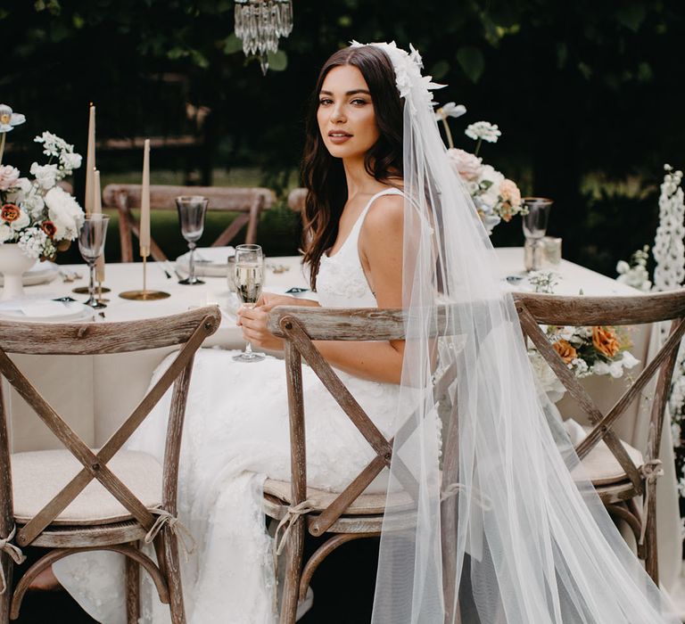 Bride sitting at an elegant outdoor table scape in a cathedral length veil with appliqué detail 