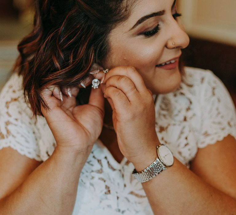 Indian bride with half up half down braided hair putting on her diamond earrings 