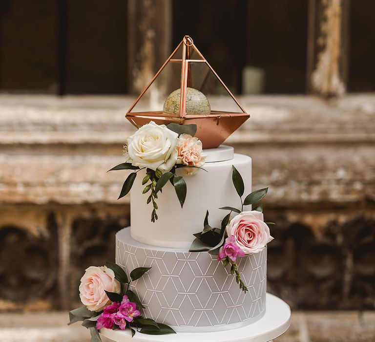 Three-tier wedding cake with grey iced tier and globe cake topper in a gold prism 