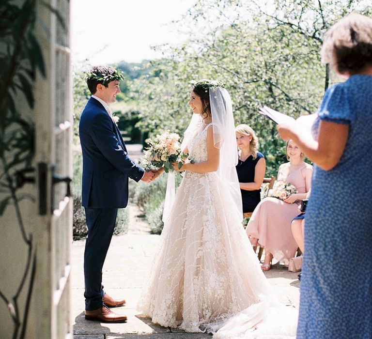 Bride & groom hold hands and look lovingly at one another during wedding ceremony