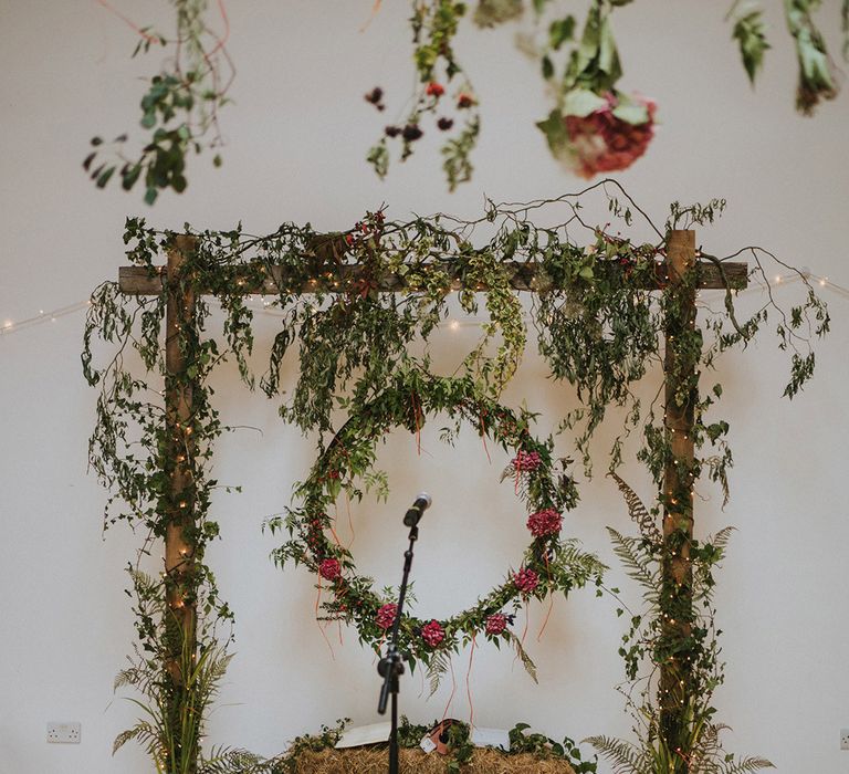 Green foliage and colourful florals around wooden archway for beach wedding