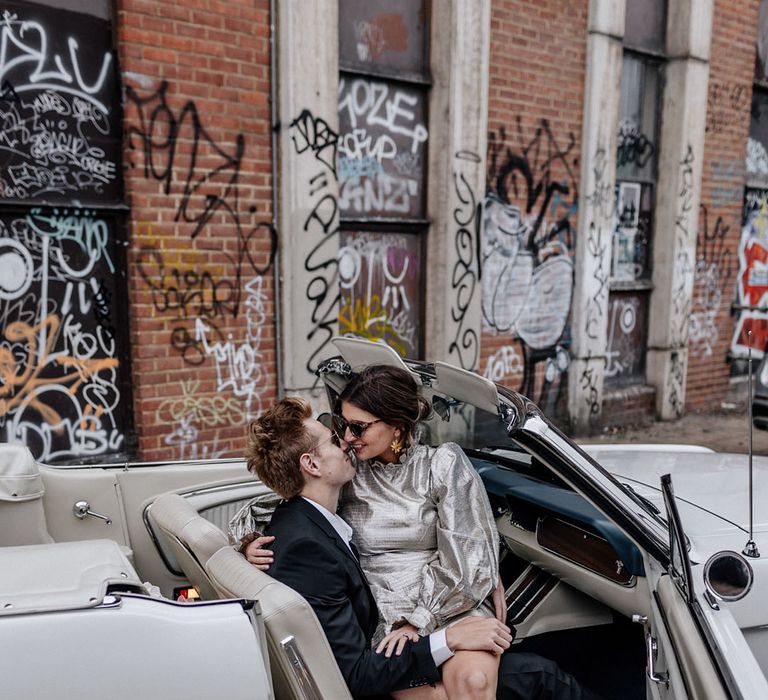 Groom and Bride kiss inside white convertible car parked by an urban graffiti wall industrial wedding 