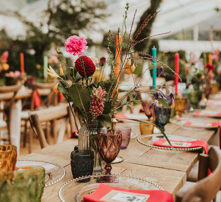 Bright wedding table decor with flower stems in bottles, coloured goblets and glass charger plates 