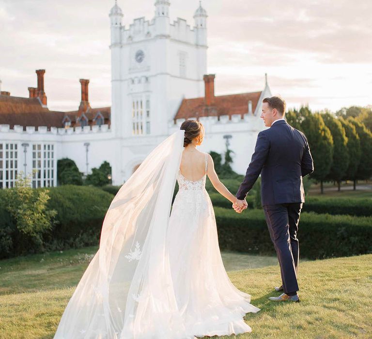 Bride & groom walk across the grounds of Danesfield house as the brides veil blows in the wind