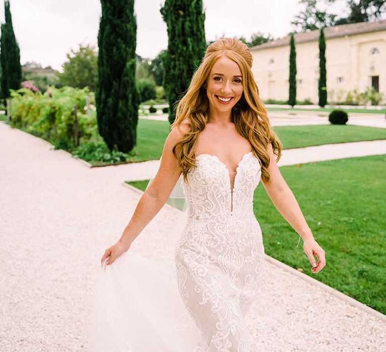 Bride walks outdoors whilst holding the train of her wedding day