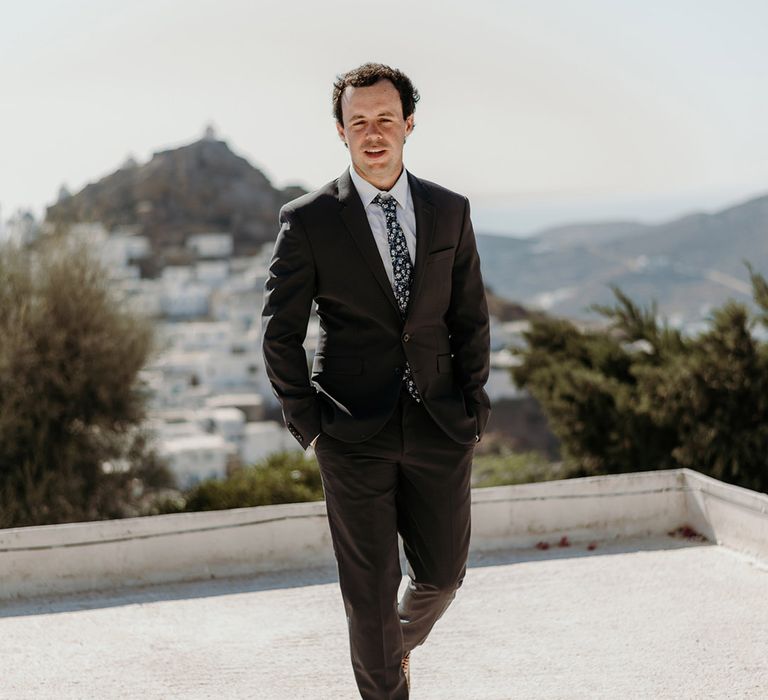 Groom walks outdoors as he wears black suit with floral tie 