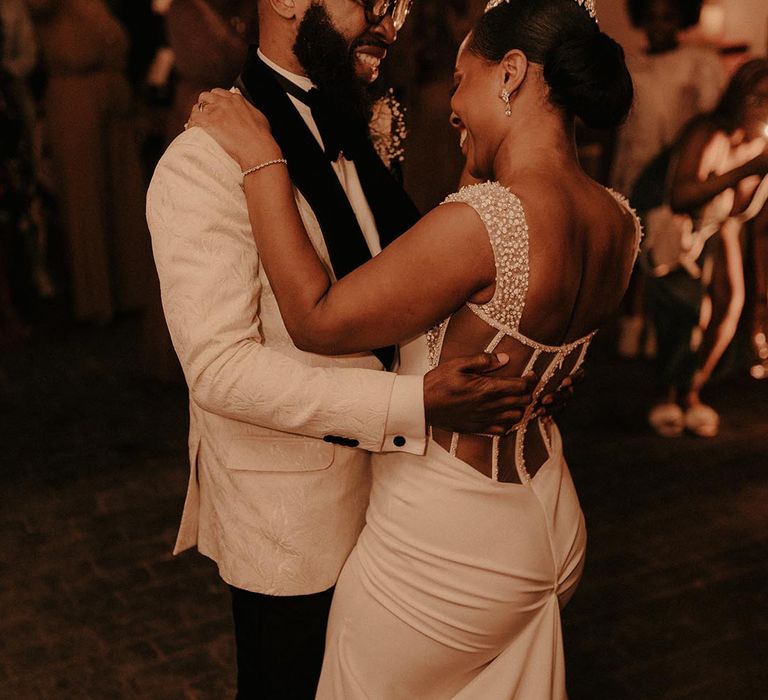 First dance with black groom in a white brocade tuxedo jacket with his bride in a boned backless wedding dress with embellishment 