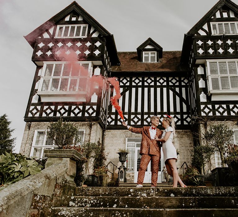 Bride in a leopard print trouser suit holding a smoke flare at fun LGBTQ+ wedding at The Highfield House, Yorkshire 