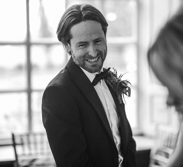 Groom wears black tie on his wedding day whilst smiling with wedding guests 