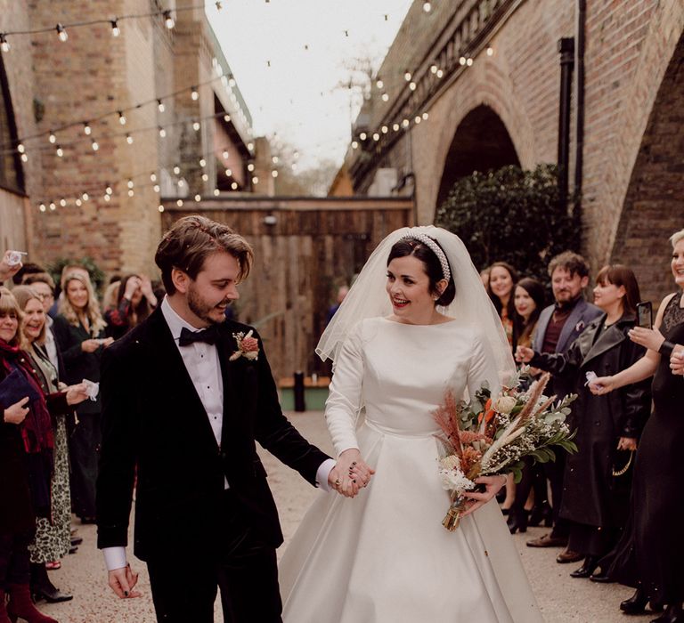 Bride and groom walk hand in hand together in front of wedding guests