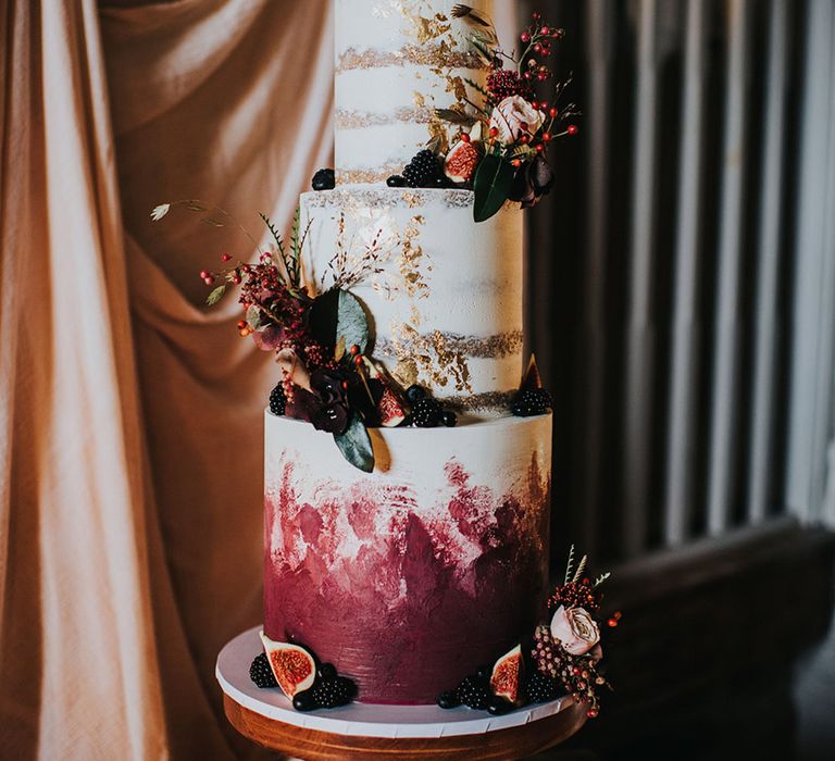 Semi naked wedding cake with burgundy, white and gold layers and decor as well as figs and fruits 