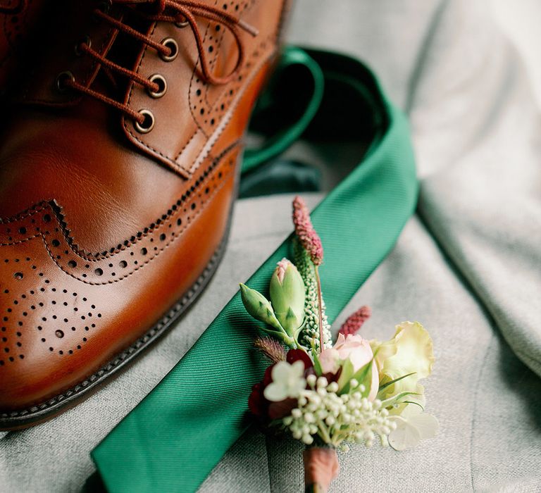 Groom's accessories including brown shoes, green tie and wildflower boutonnière with his bespoke grey suit 