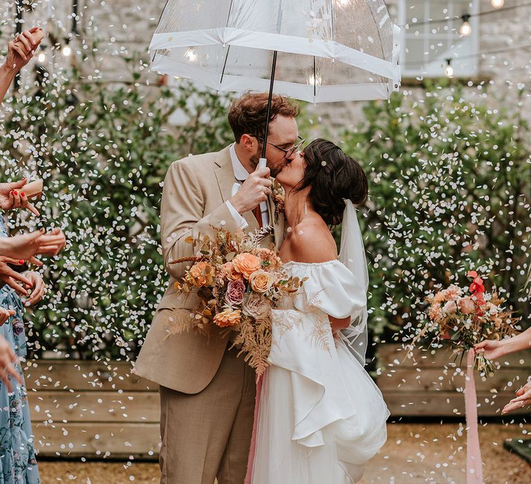 Bride and groom get their confetti exit with bride in Loeffler Randall wedding shoes and groom holding clear umbrella