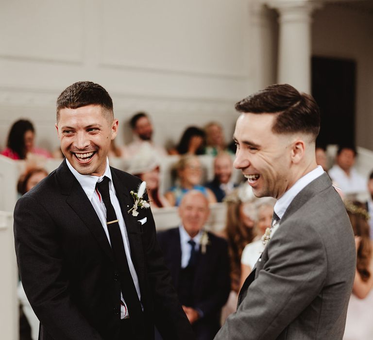 Smiling grooms holding hands at the altar on their wedding day