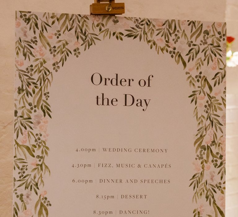 Order of the day wedding sign with leaf design and pink flowers on wooden easel