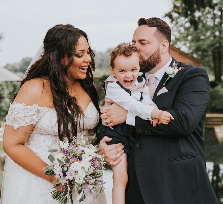 Bride and page boy laugh together as the groom kisses him on the cheek