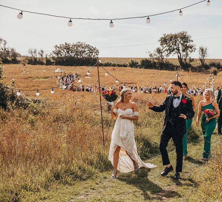 Bride and groom lead their large party of wedding guests to the reception after their outdoor wedding ceremony