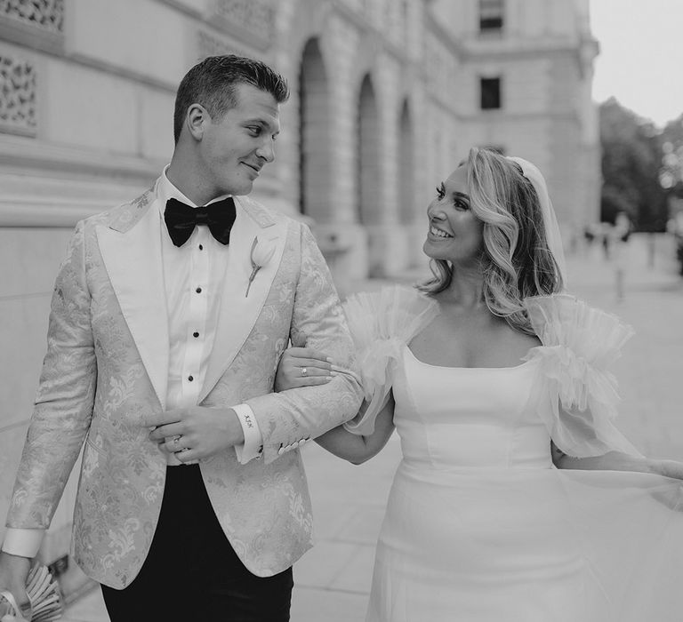 Bride in Halfpenny London smiles at groom in custom tuxedo and personalised shirt cuffs with initials