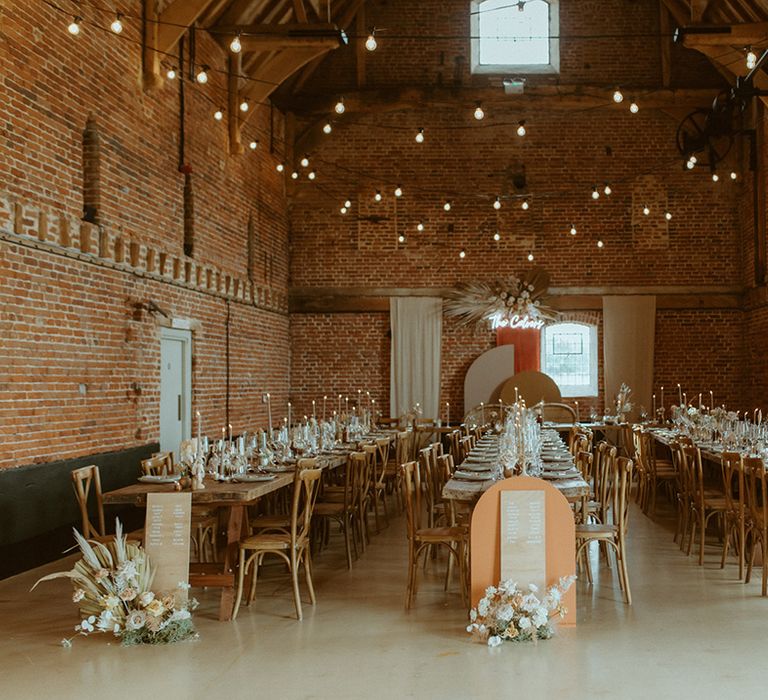 Barn wedding venue with long wooden banquet tables with wooden seating chart signs next to the tables and neon light sign decor 