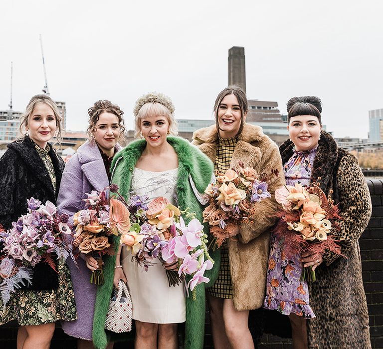 Bride with bridesmaids all in fur coats of different styles and patterns holding purple and orange wedding bouquets