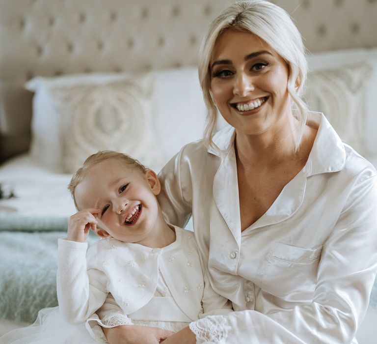 Bride in white satin pyjamas with daughter in white tulle dress and white pearl cardigan 