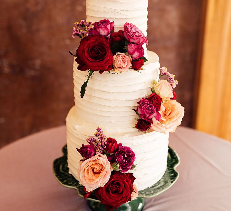 Three tier white frosted wedding cake with textured pattern with red flowers decorating the cake 