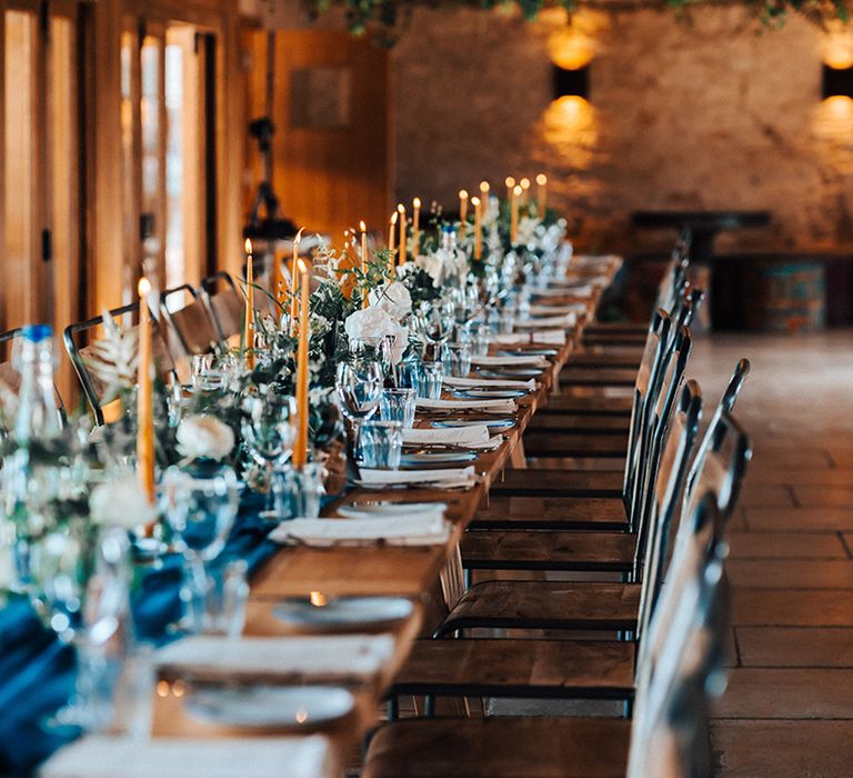 Wedding table setting with blue glassware and table runner with mustard candles at rustic barn venue 