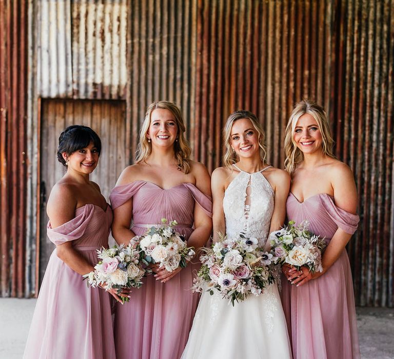 Bridesmaids in pink off the shoulder dress with bride in halter neck wedding dress with pink and white bouquets 