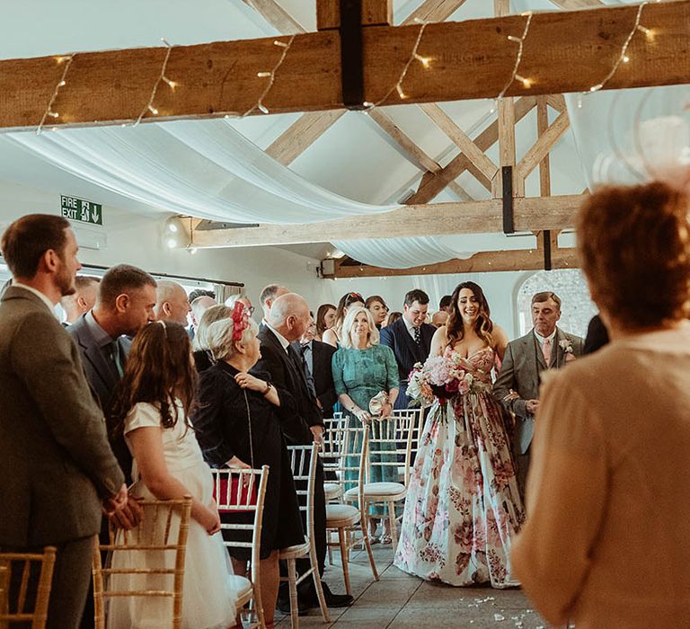 Father of the bride in a grey suit with a pink tie walks the bride in a pink flower wedding dress down the aisle 