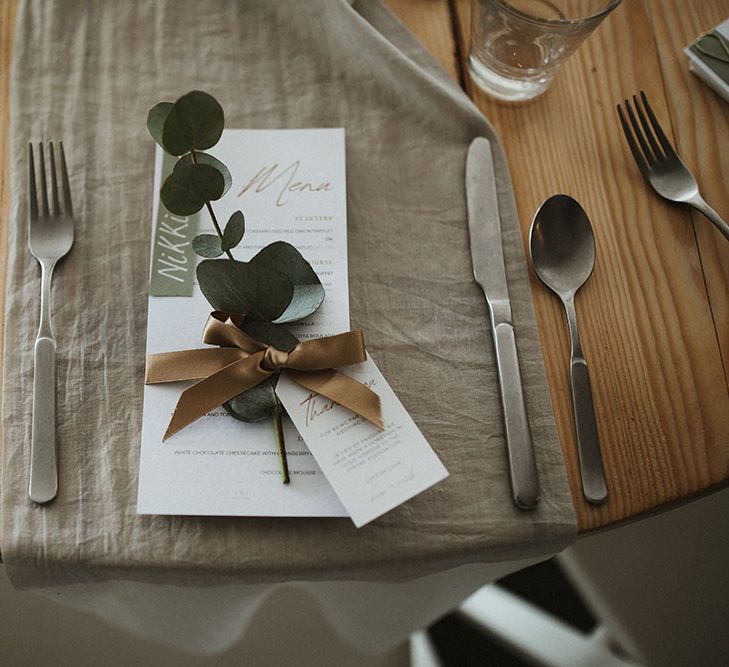 Sage green fabric table runner on wooden table with white stationery tied with brass coloured silk ribbon