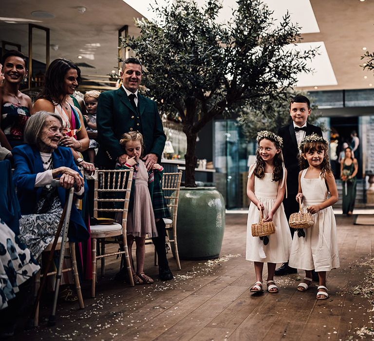 Flower girls with white dresses and white sandals with a page boy in black tie walk down the aisle for wedding at Callow Hall