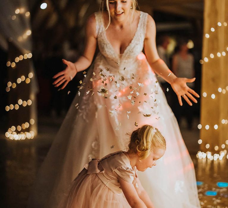 Bride in a lace beaded wedding dress throws confetti over a little girl in a pink tulle dress