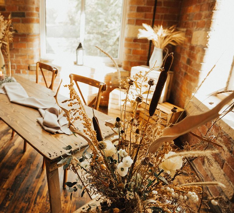 Dried floral arrangements beside wooden table and neutral table runner 