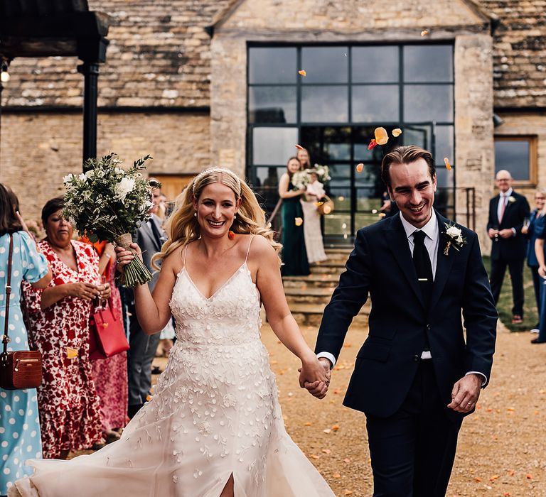 Bride in an Alexandra Grecco Lana wedding dress and groom in a dark blue suit have their confetti moment after the ceremony 