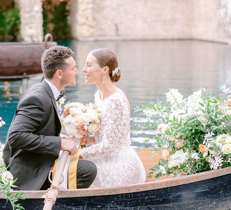 The bride and groom sit in a row boat together surrounded by yellow wedding flowers 