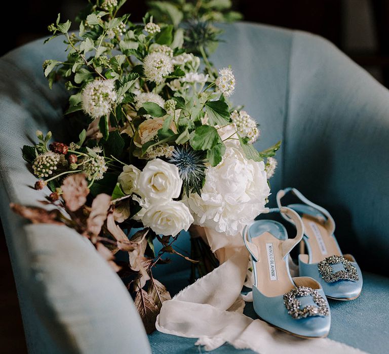 Something blue wedding shoes by Manolo Blahnik resting on a blue chair with the Bride’s bouquet made of roses, thistles and other wildflowers