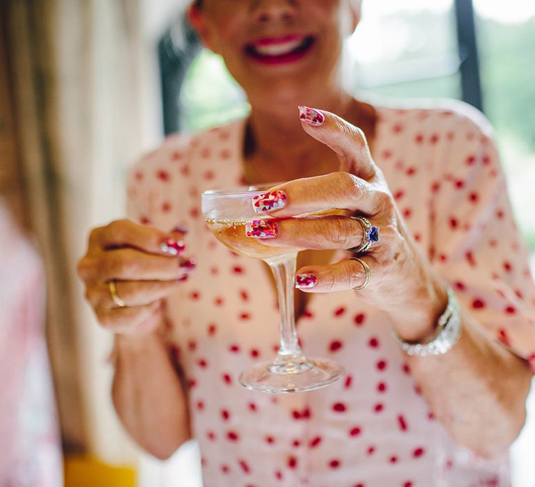 Mother of the bride with glittery heart nails and matching pink and red polka dot satin pyjamas holding a glass of champagne 