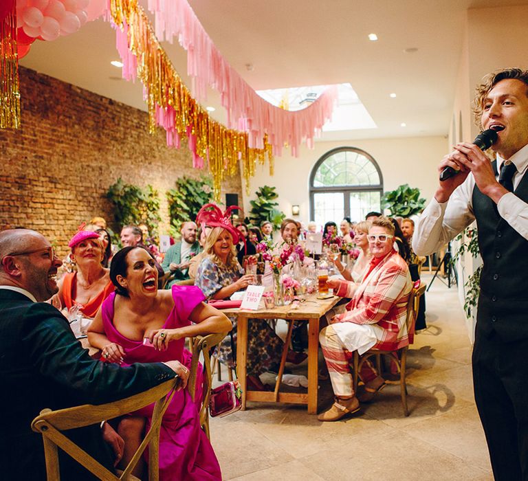 Waiter in black waistcoat and trousers singing to wedding guests in Middleton Lodge reception room with pink and gold wedding streamers 