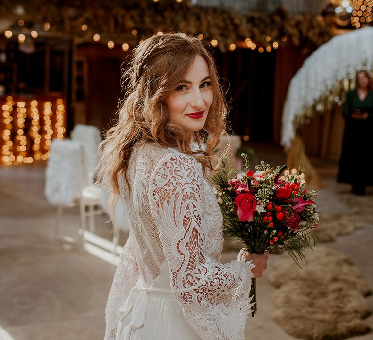 Bride in long sleeve lace wedding dress with tassels, sheer open back detail and white ribbon tie holding rose, baby's-breath, peony and dried flower bouquet 