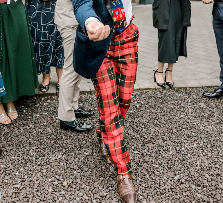 Wedding guest wears red tartan trousers with blue velvet jacket with multicoloured tie 