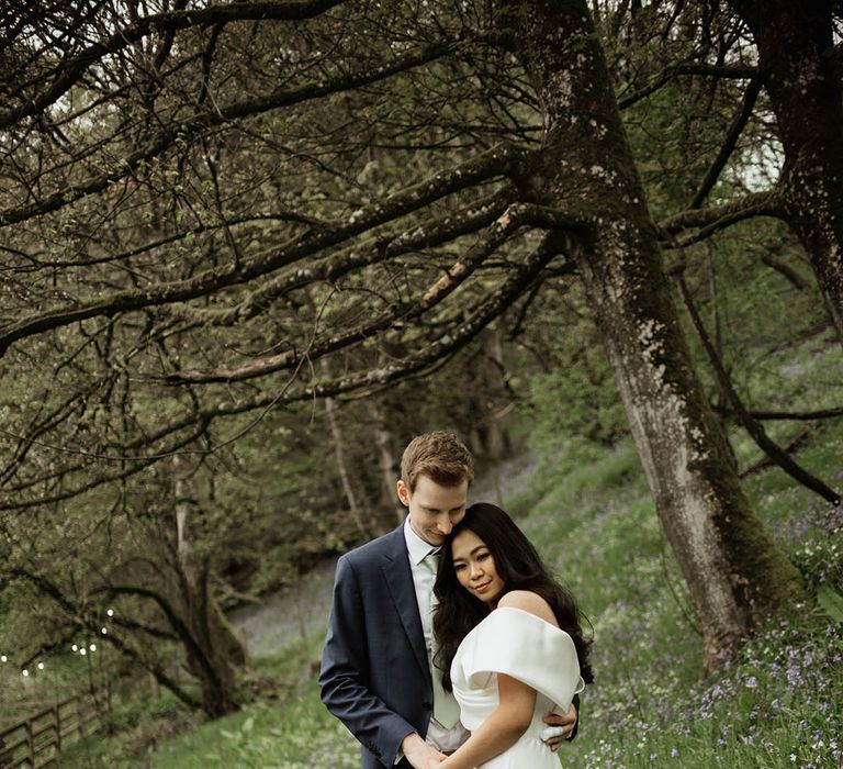 Groom in navy suit rests his head against the bride as they embrace in a romantic meadow at Hidden River Cabins 